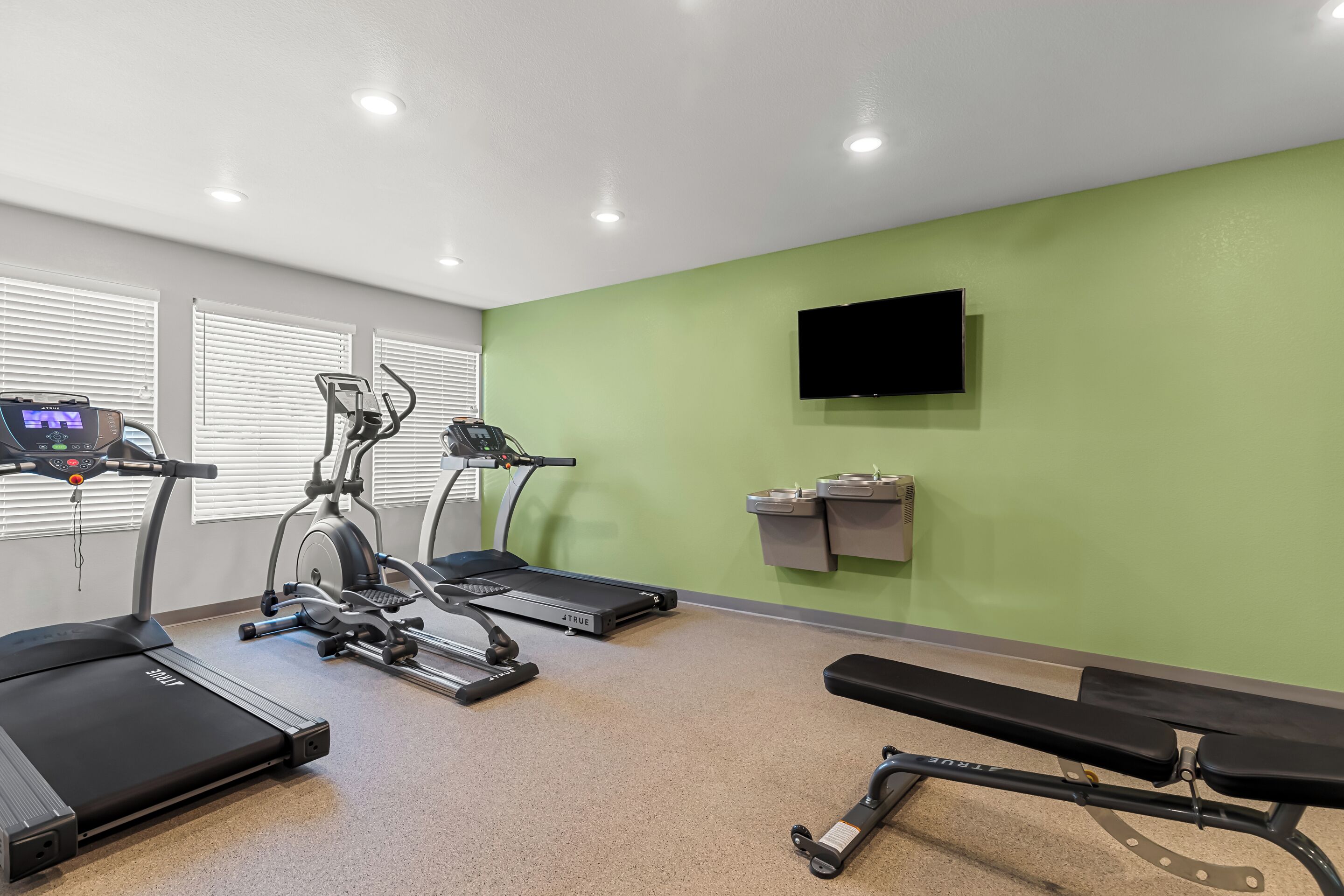 A fitness room with treadmills, an elliptical, and a bench.