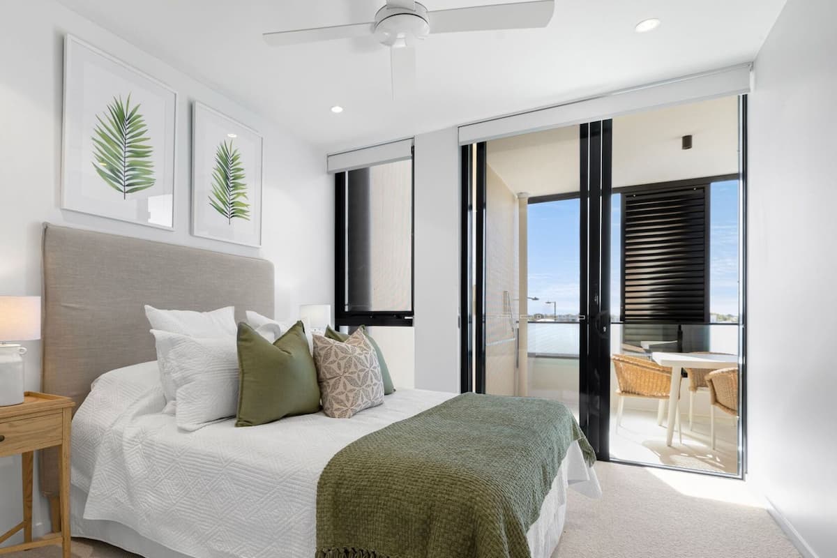 Relax in this serene bedroom with a large bed, nightstand, and bedside table, featuring a ceiling fan and sliding glass door to an outdoor area.