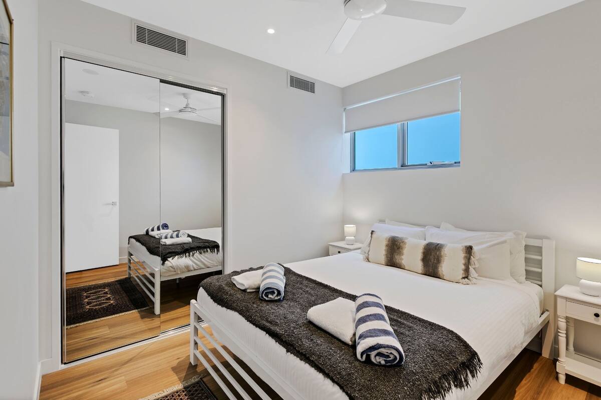 Un dormitorio moderno con una cama grande, una mesita de noche, un espejo y una ventana.