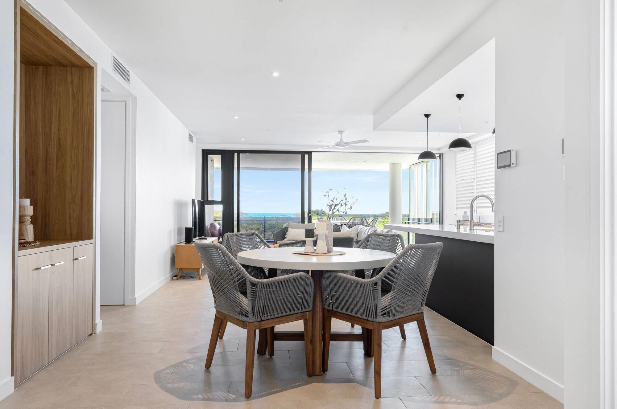 Een moderne keuken met een groot eiland, een eethoek met rieten stoelen en uitzicht op de omgeving.