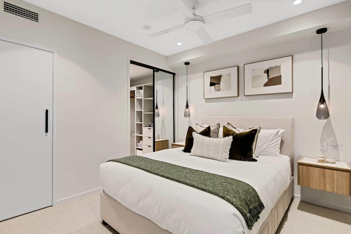 Un dormitorio con cama, mesitas de noche, un armario, ventilador de techo y obras de arte en la pared.