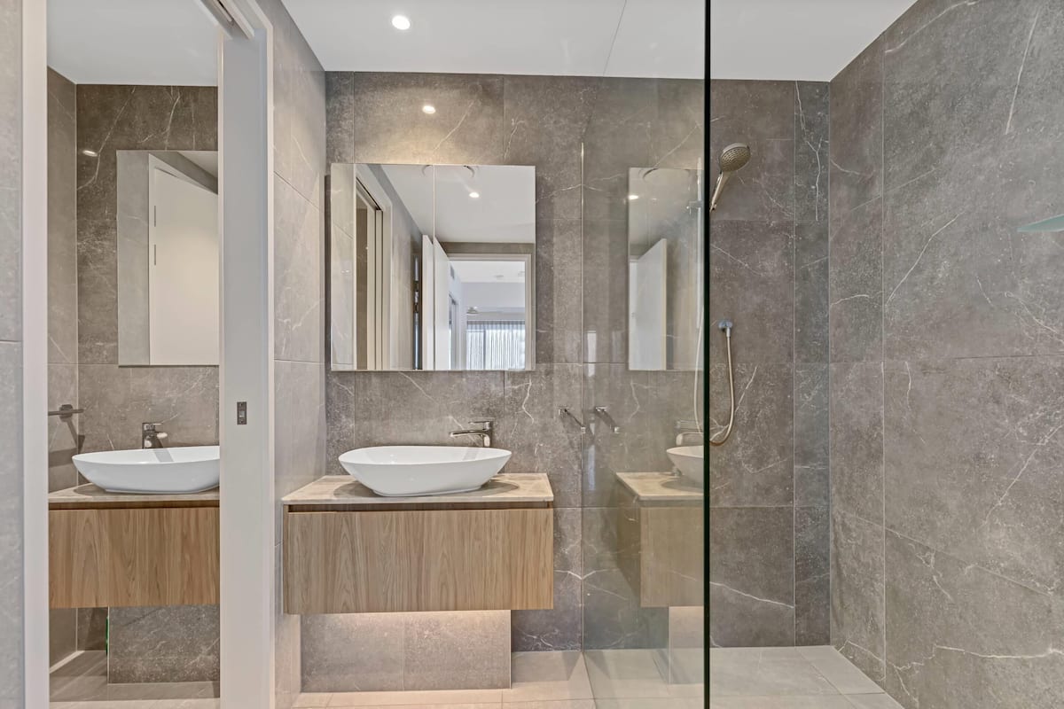 Un baño moderno con dos lavamanos, una cabina de ducha de vidrio y paredes de mármol.