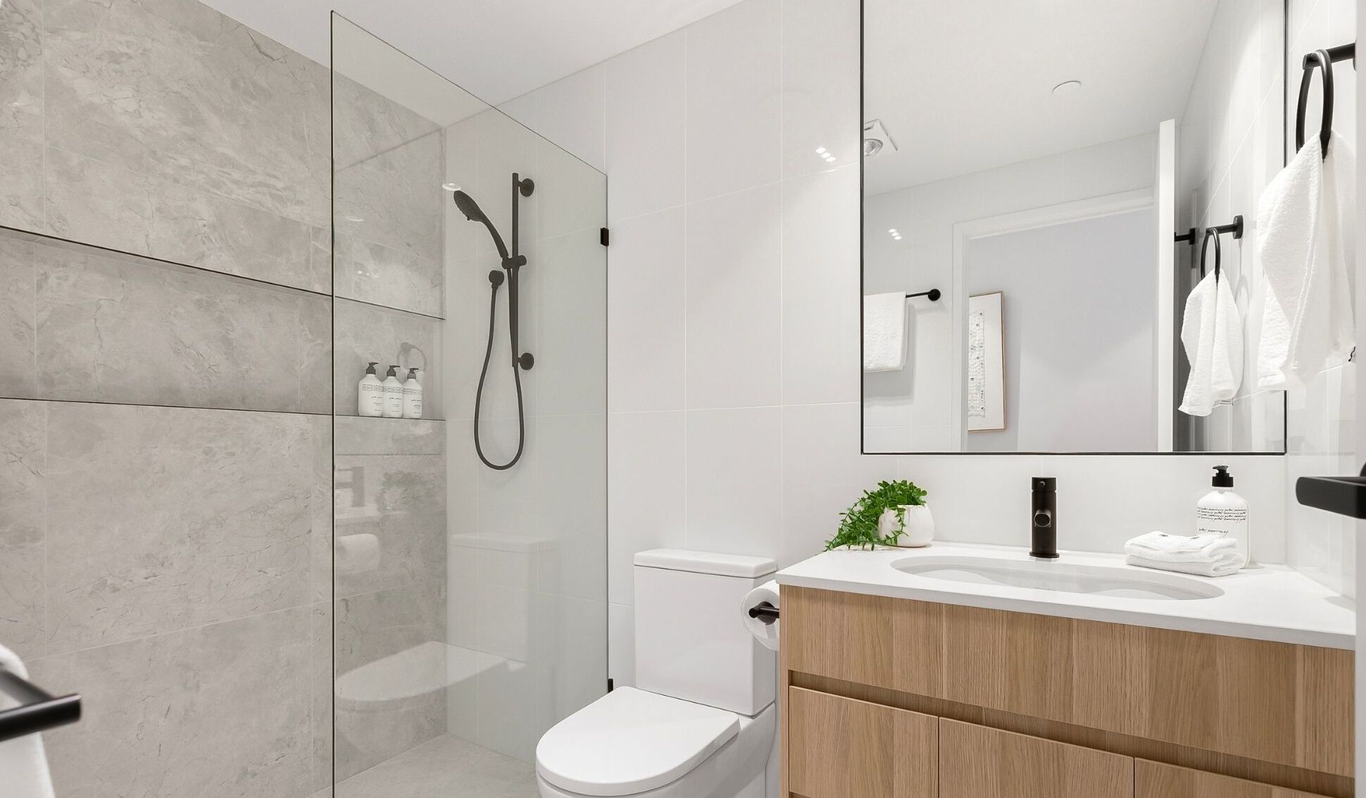 A modern bathroom with a glass-enclosed shower, a toilet, and a vanity with a mirror.