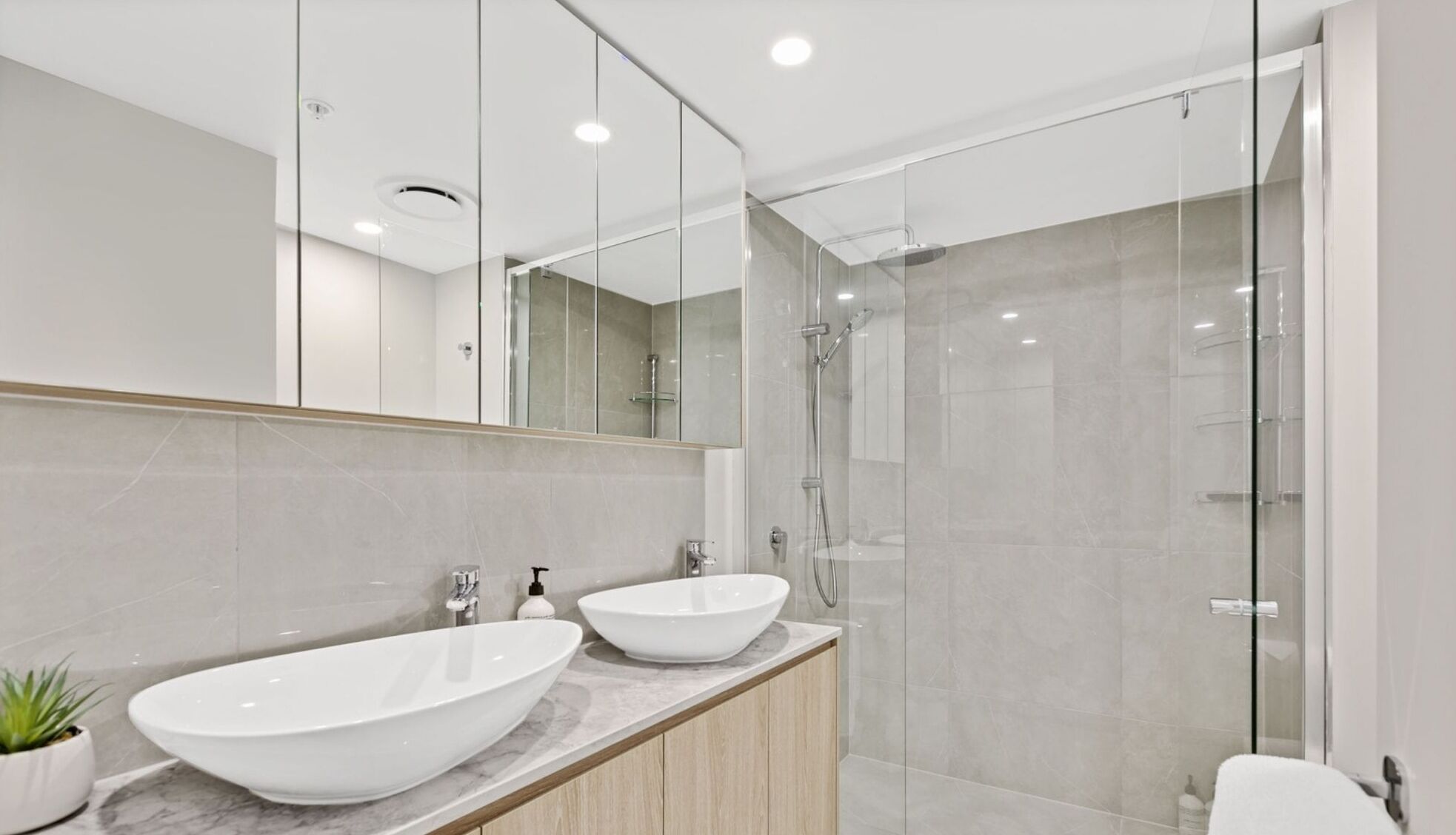 Een moderne badkamer met een grote spiegel, twee wasbakken en een douche met glazen wanden.