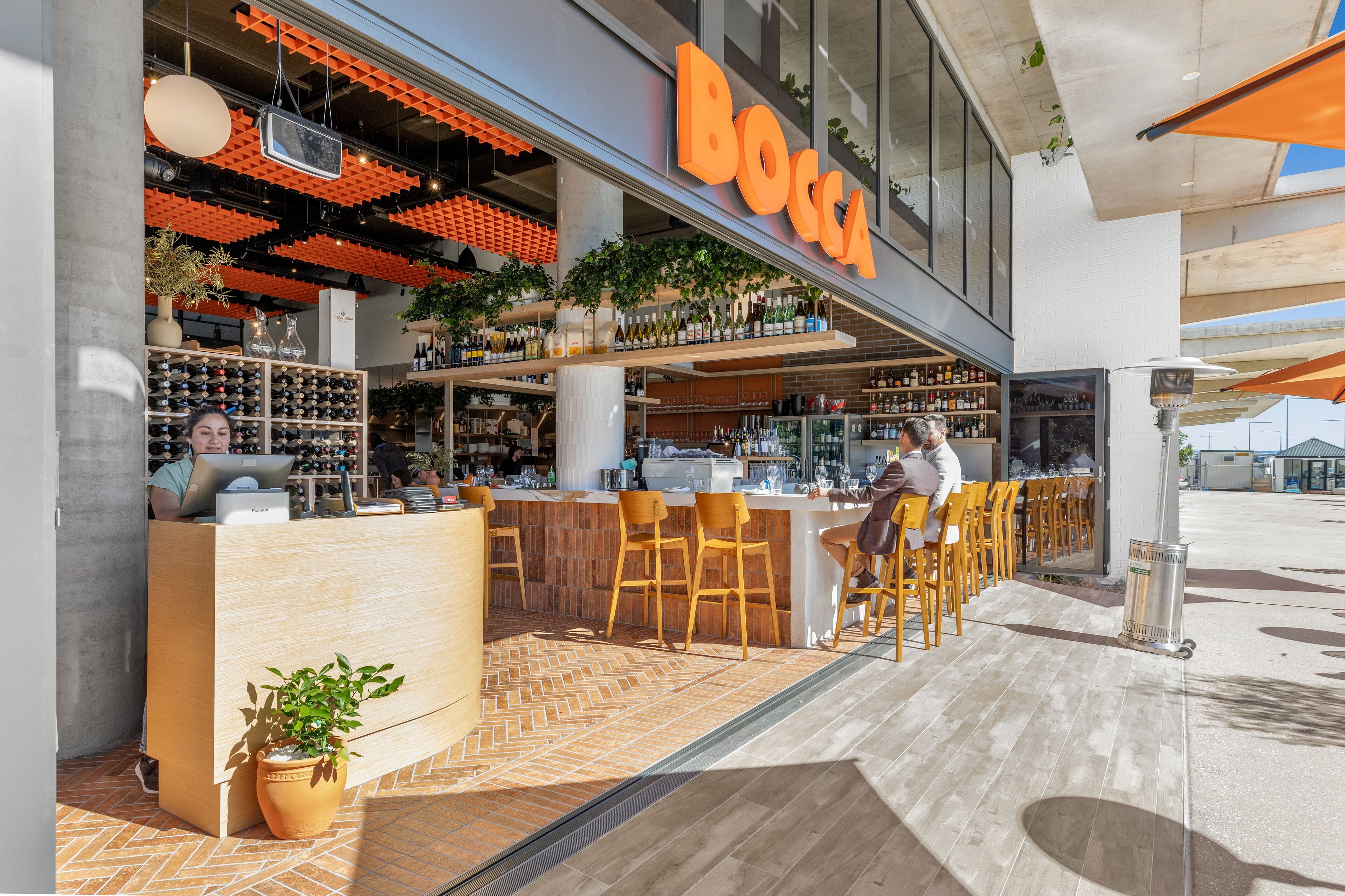 A bar area with a counter, bar stools, and a variety of bottles on shelves.