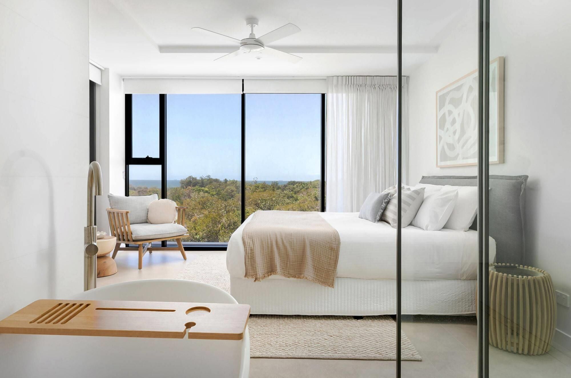 A modern bedroom with a large bed, a chair, a desk, and a view of the outdoors.