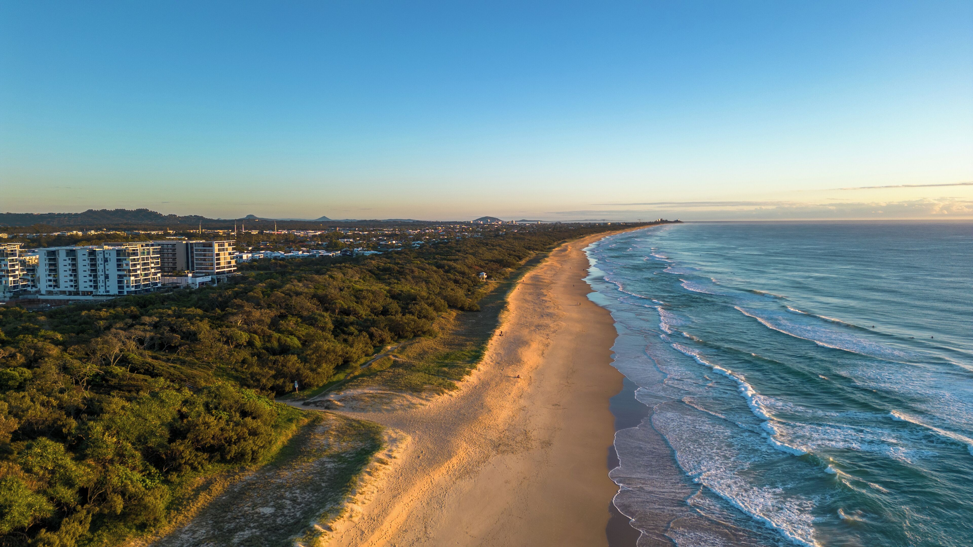 Une zone côtière comprenant une plage de sable, une forêt dense et une rangée d’immeubles à plusieurs étages.