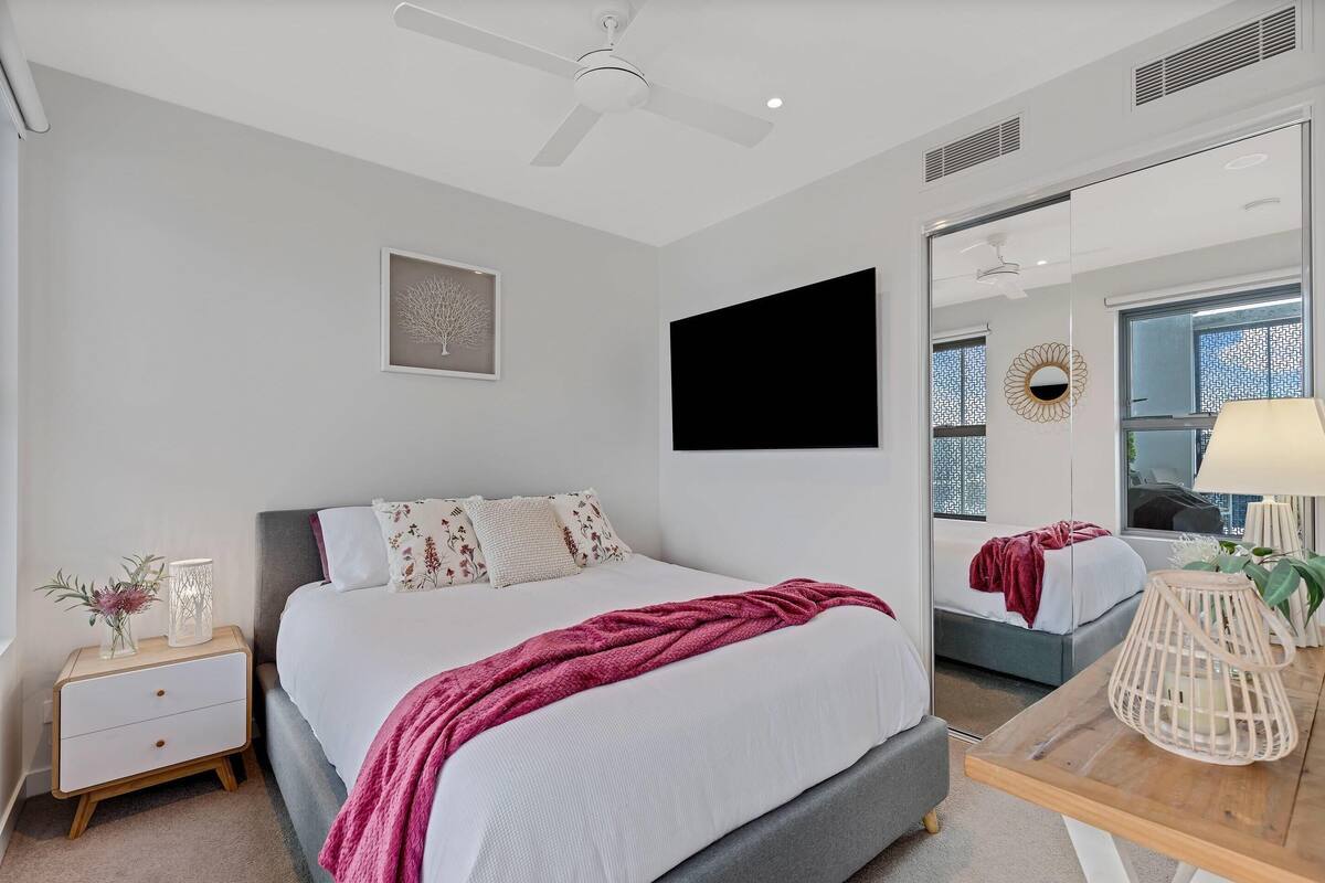 Un dormitorio con cama, mesita de noche, lámpara y un espejo grande.