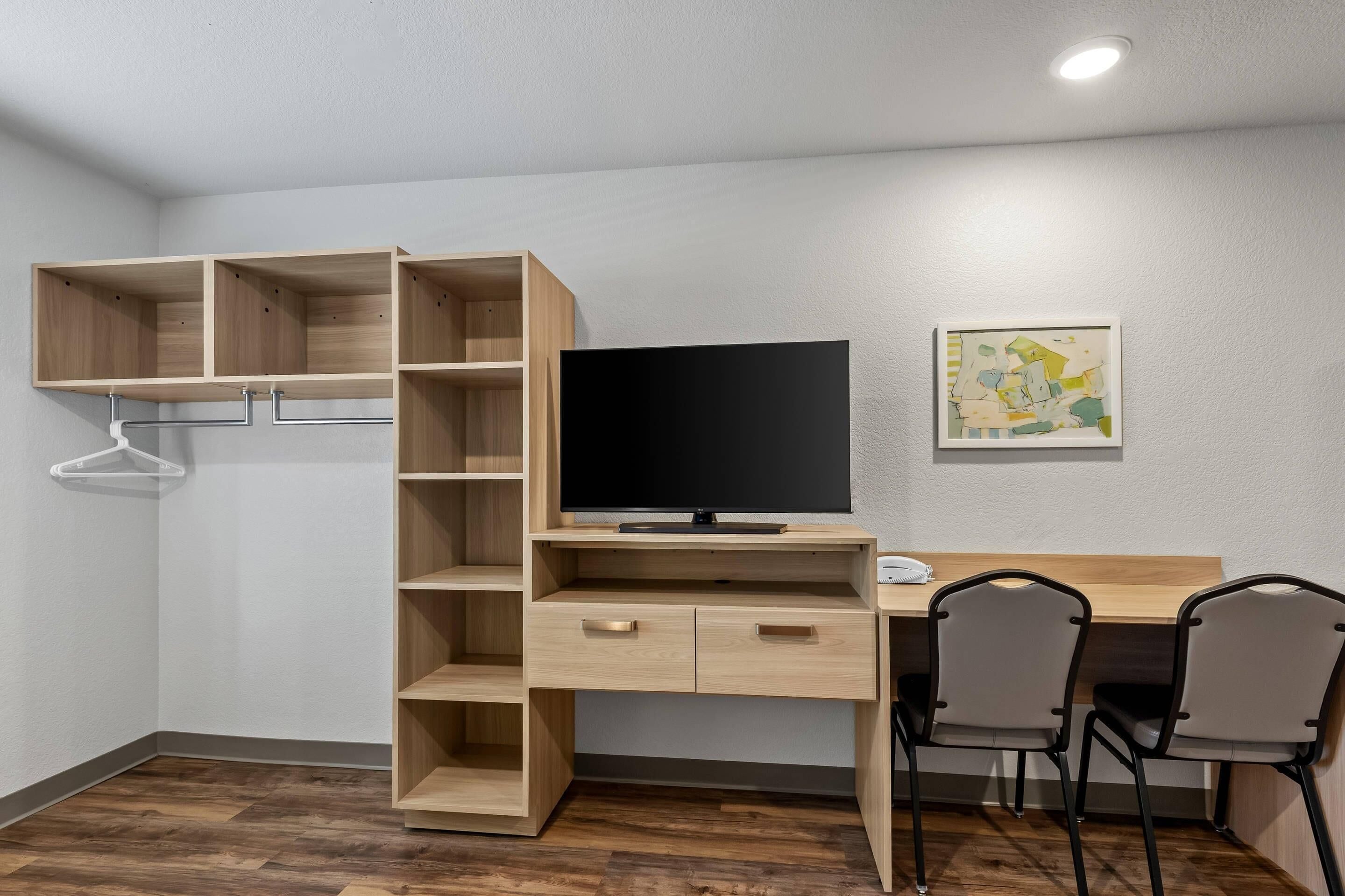 A room with a wooden desk, two chairs, a television, and a wall-mounted shelf.