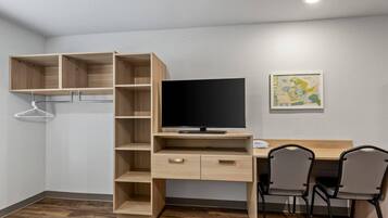 A room with a wooden desk, two chairs, a television, and a wall-mounted shelf.