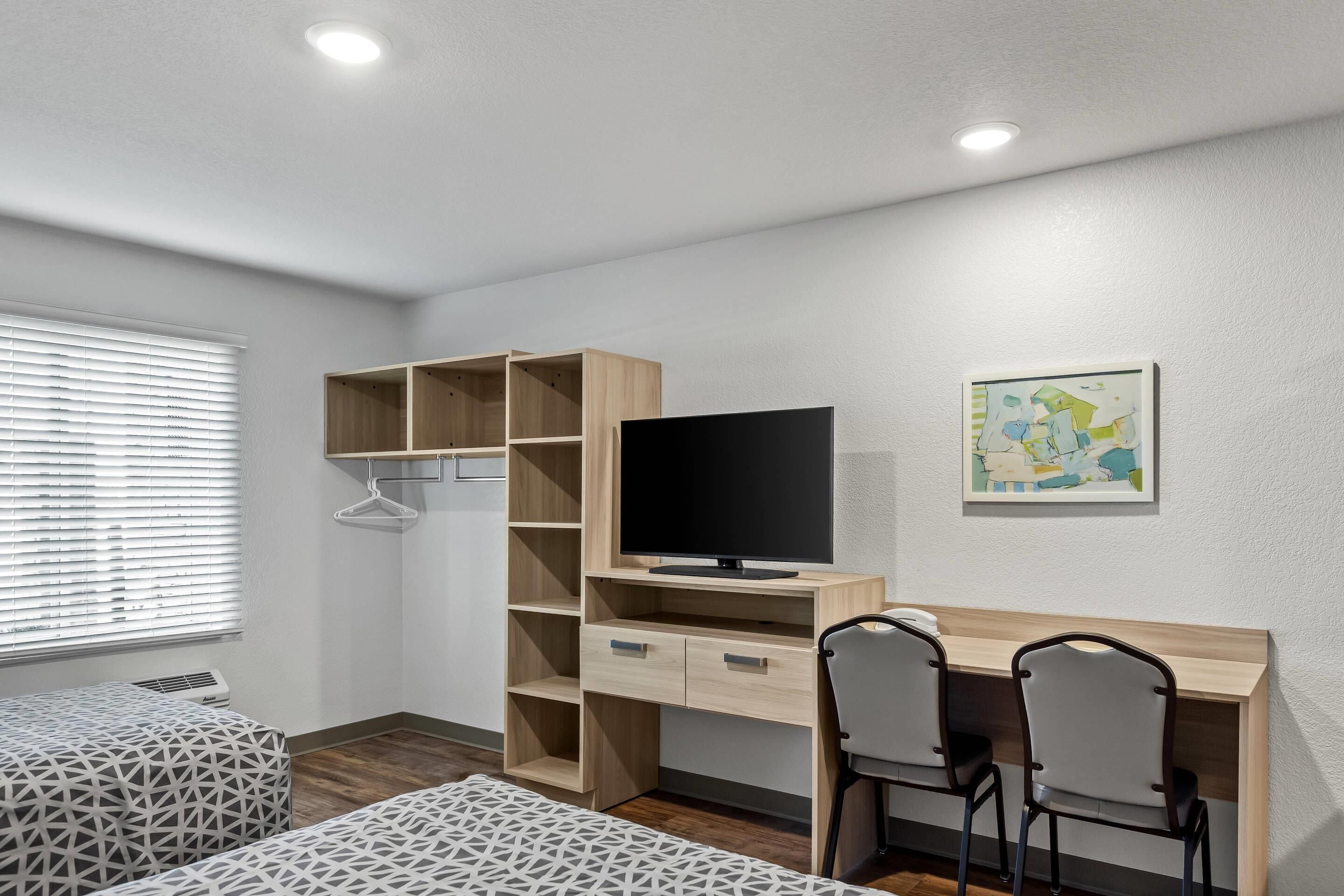 Een slaapkamer met een houten bureau, twee stoelen, een televisie en een kaart aan de muur.