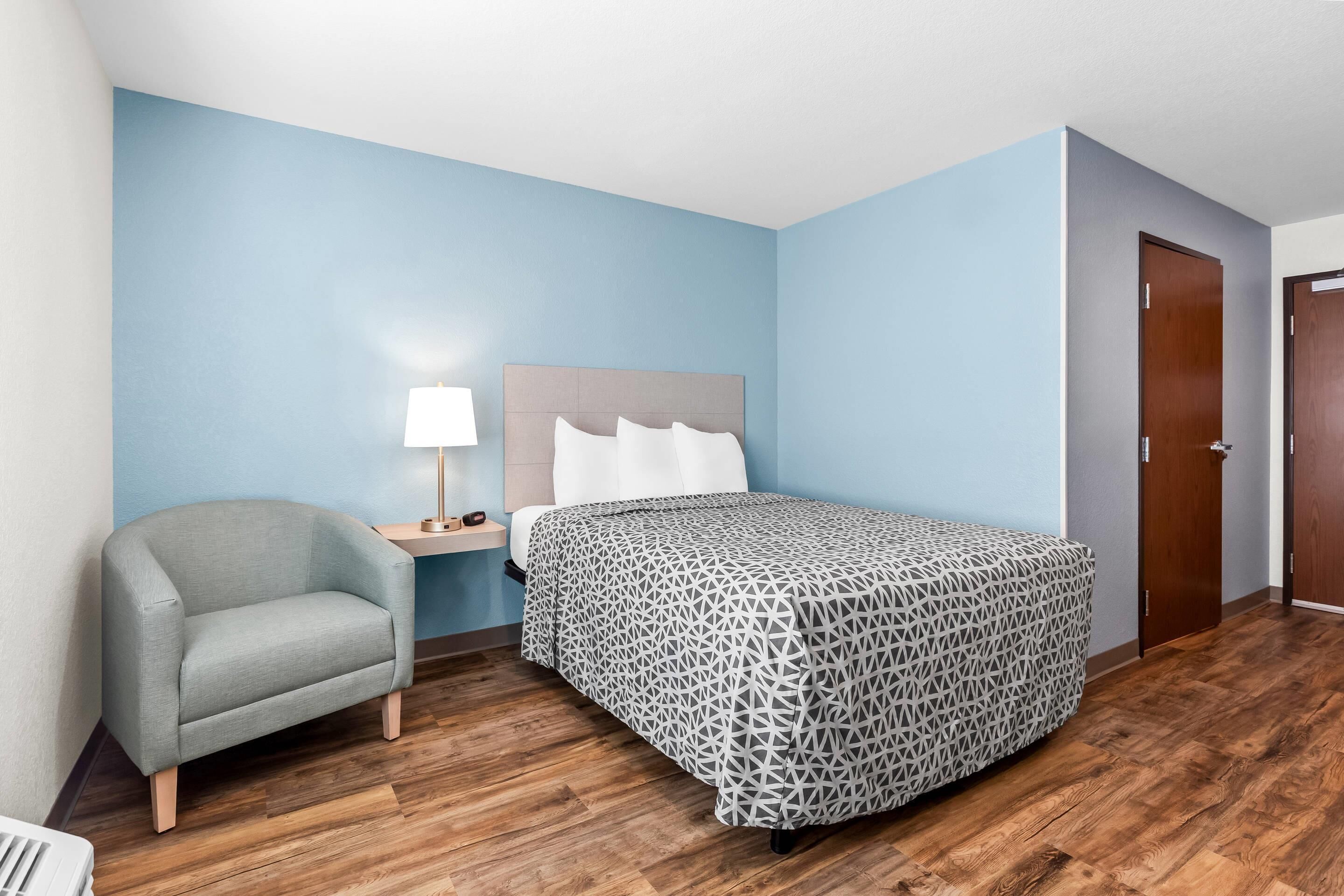 Een hotelkamer met een bed, een stoel, een nachtkastje en een lamp.