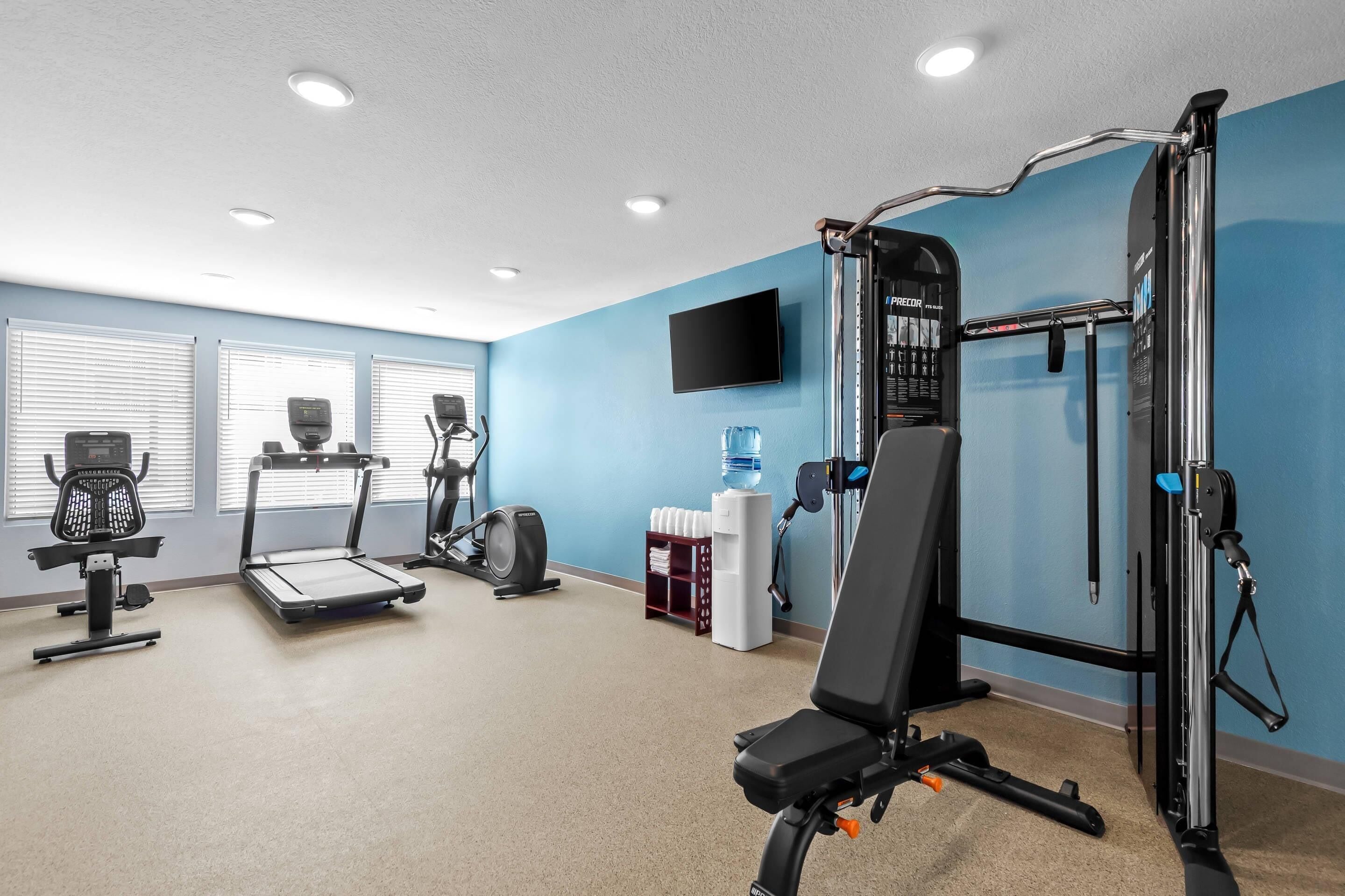 Un gimnasio con equipo de ejercicio, dispensador de agua y televisor en la pared.