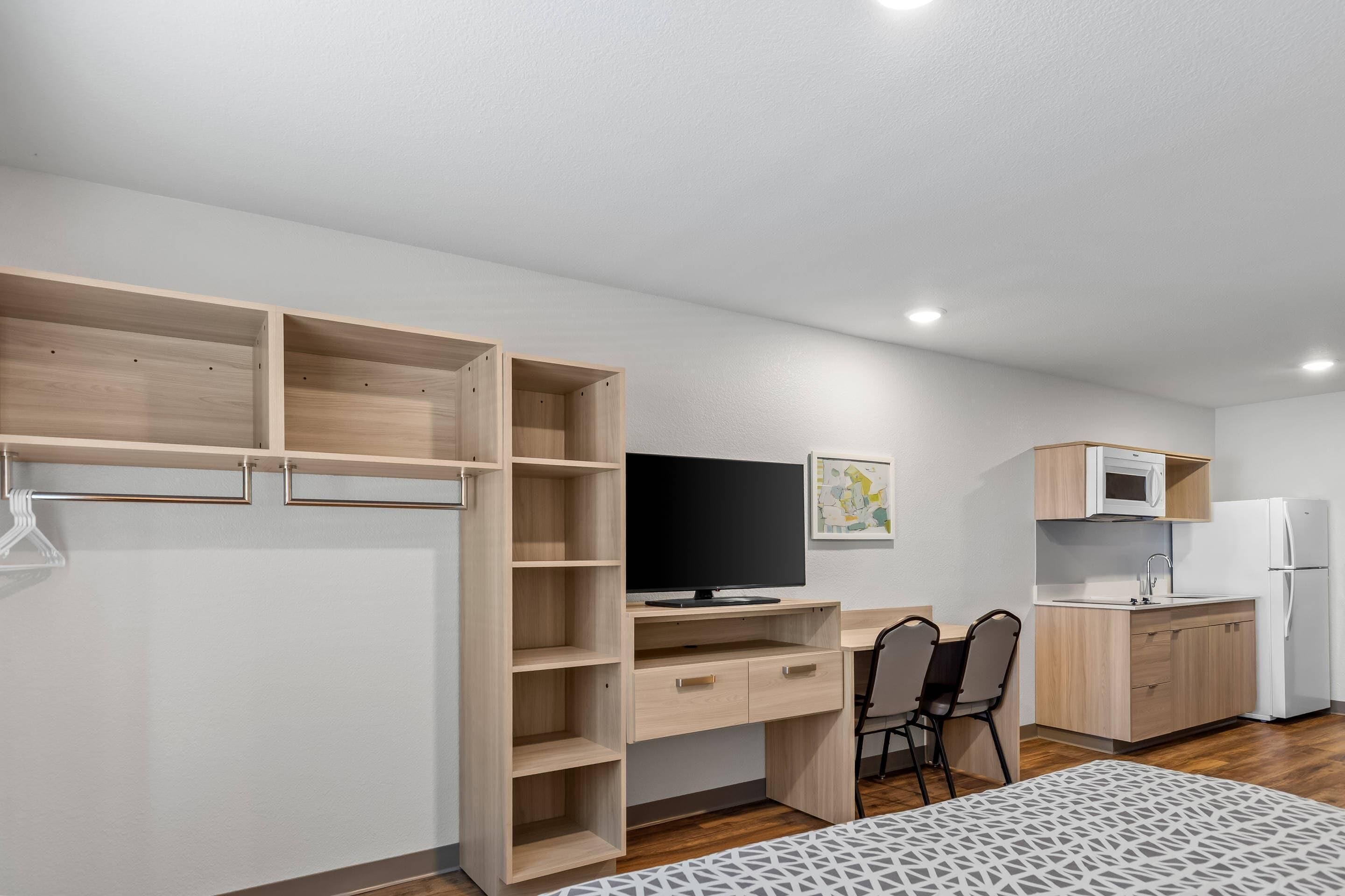 Una habitación compacta con una cama, un escritorio con computadora, una silla, un televisor, un microondas y un refrigerador.