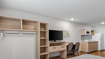 A compact room with a bed, a desk with a computer, a chair, a TV, a microwave, and a refrigerator.