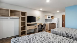 A compact hotel room with two beds, a desk with a chair, a television, a microwave, and a refrigerator. - WoodSpring Suites St Peters-OFallon (St. Peters)