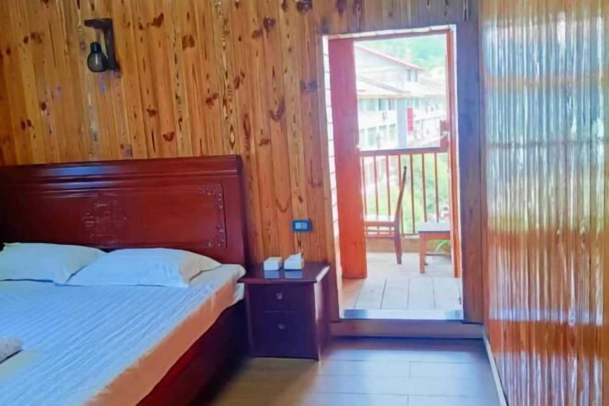 A wooden room with a bed, a nightstand, and a door leading to an outdoor area.