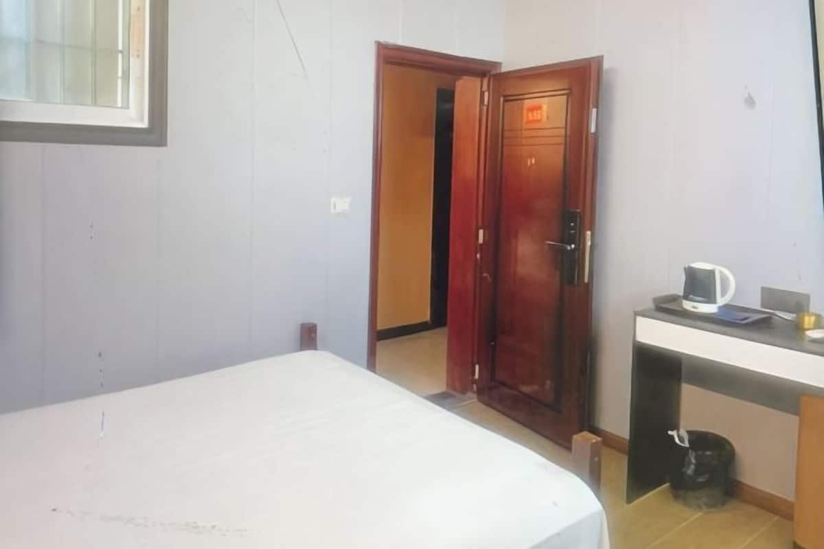 A bedroom with a bed, a wooden door, a desk with a cup, and a trash bin.