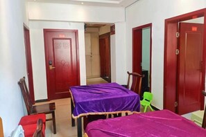 A hotel room with two beds, a wooden chair, a small table, and a red door. - Yingbin Inn (Chongqing)