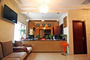 Rebedor d'hotel amb taulell de recepció, zona de seients i televisió penjada a la paret.