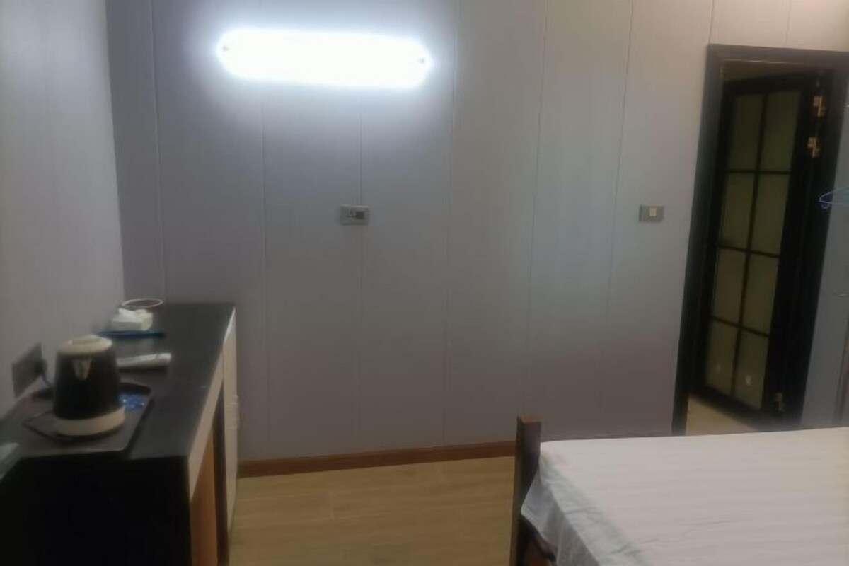 Habitació d'hotel amb llit, escriptori amb una paperera i llum penjant lluminosa.