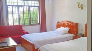 Ein Hotelzimmer mit zwei Betten, einem roten Sofa, einem Schreibtisch und einem Fenster mit Vorhängen.