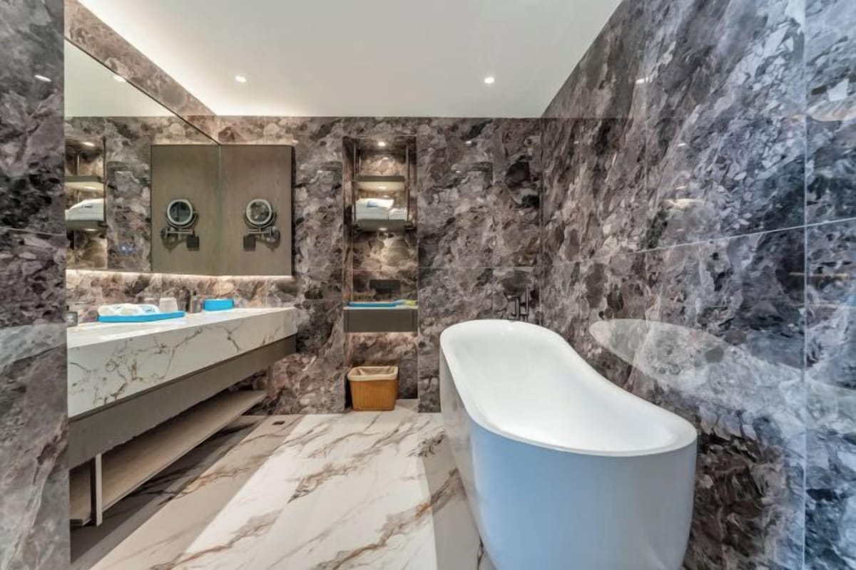A modern bathroom with a marble wall, a freestanding bathtub, and a vanity with a mirror.