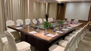 A conference room with a long table, chairs, microphones, and a projector screen.