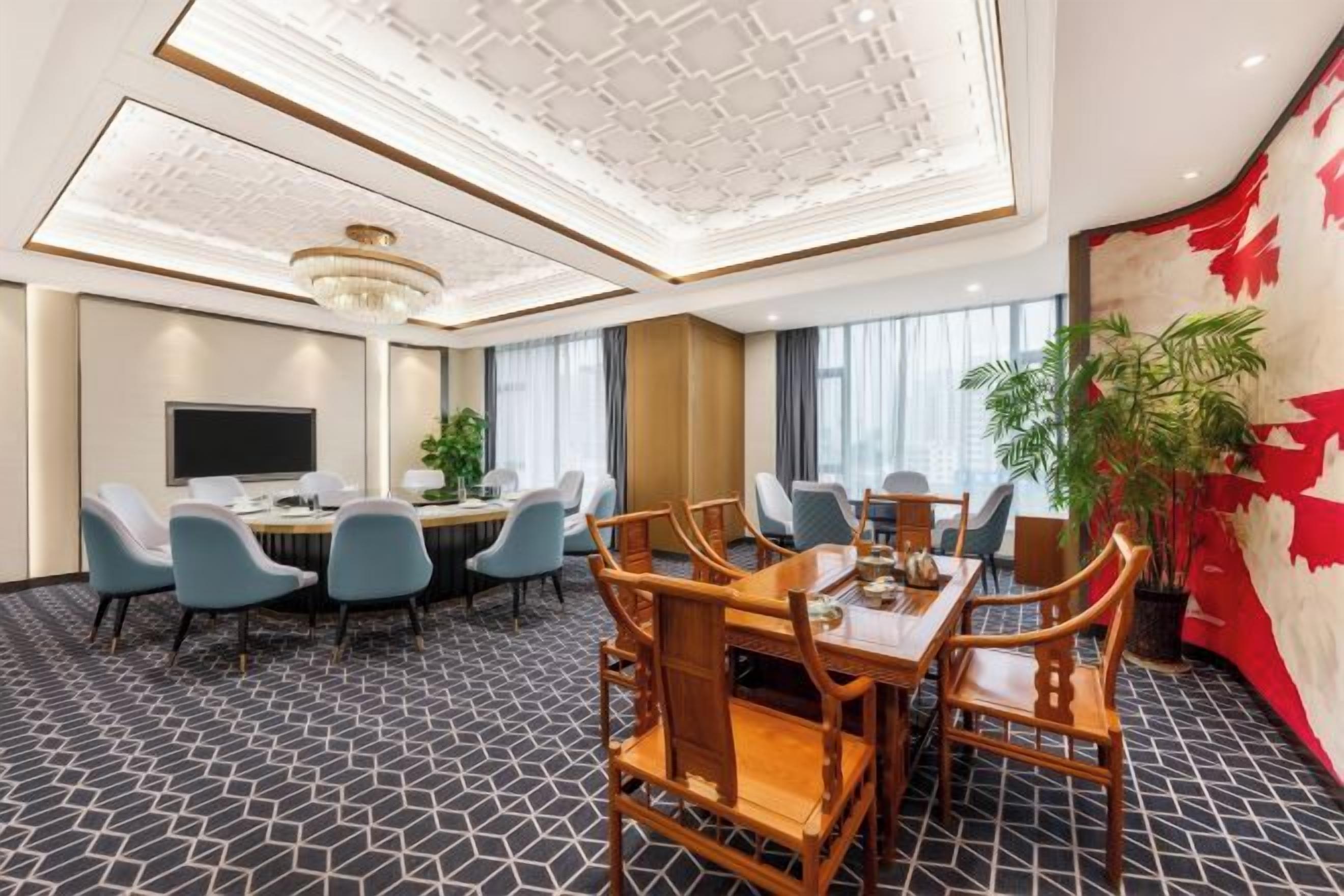A hotel conference room with a large table, multiple chairs, a television, and a plant.