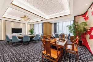 Un salón de conferencias de hotel con una gran mesa, varias sillas, un televisor y una planta.