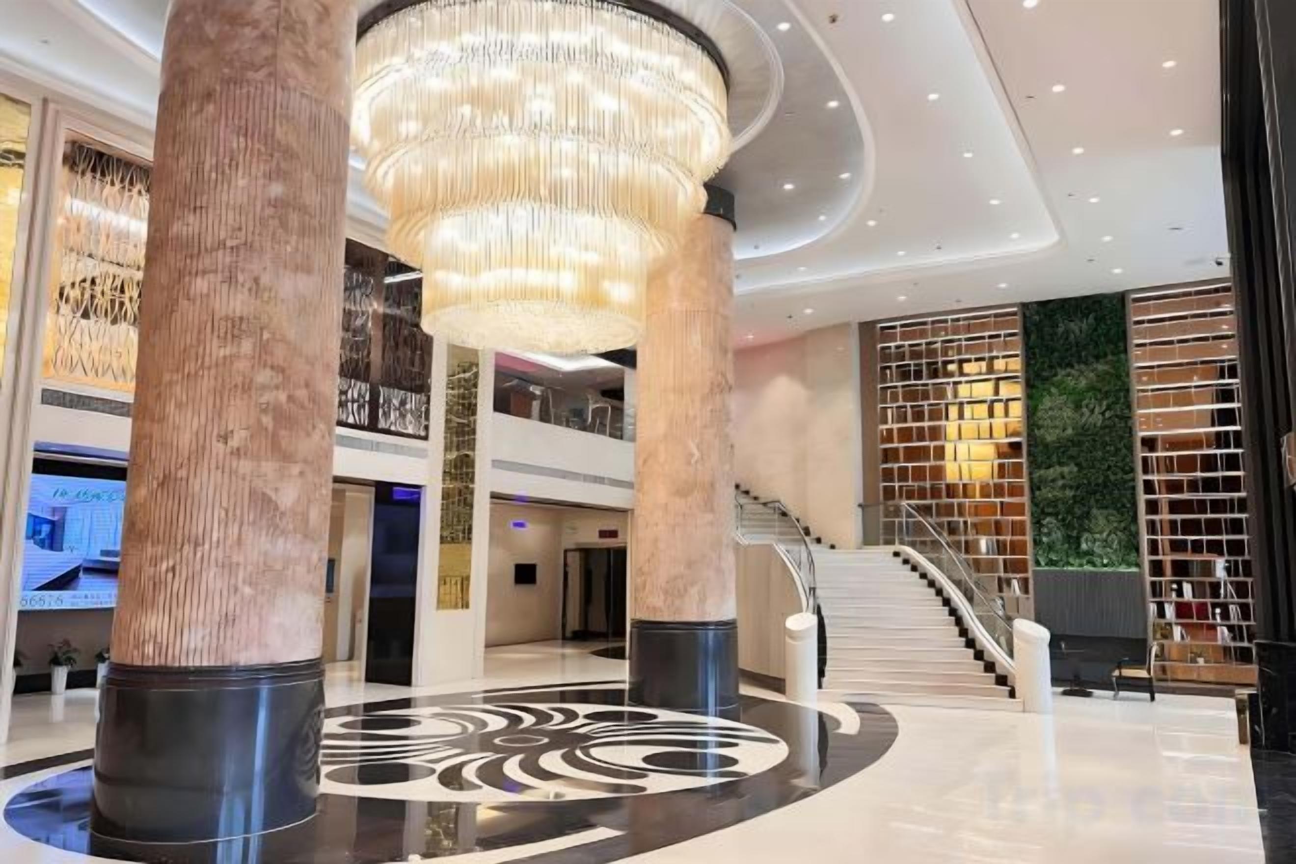 A modern lobby with a grand chandelier, a staircase, and a wall with a patterned design.