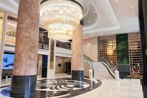 A modern lobby with a grand chandelier, a staircase, and a wall with a patterned design.