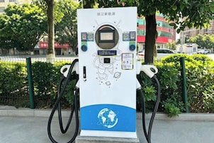 Estación de carga pública para vehículos eléctricos con pantalla digital, puertos de carga y diseño de globo en la base.