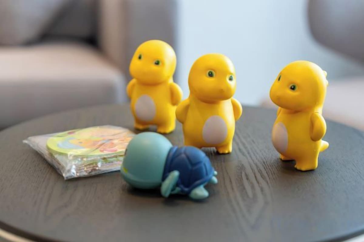 Tre gula figurer står på ett runt bord tillsammans med en blå leksak och en bok.