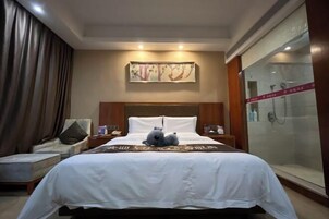 Habitación de hotel con una cama grande, una silla, una mesita de noche, un cuadro en la pared y un box de ducha de vidrio.