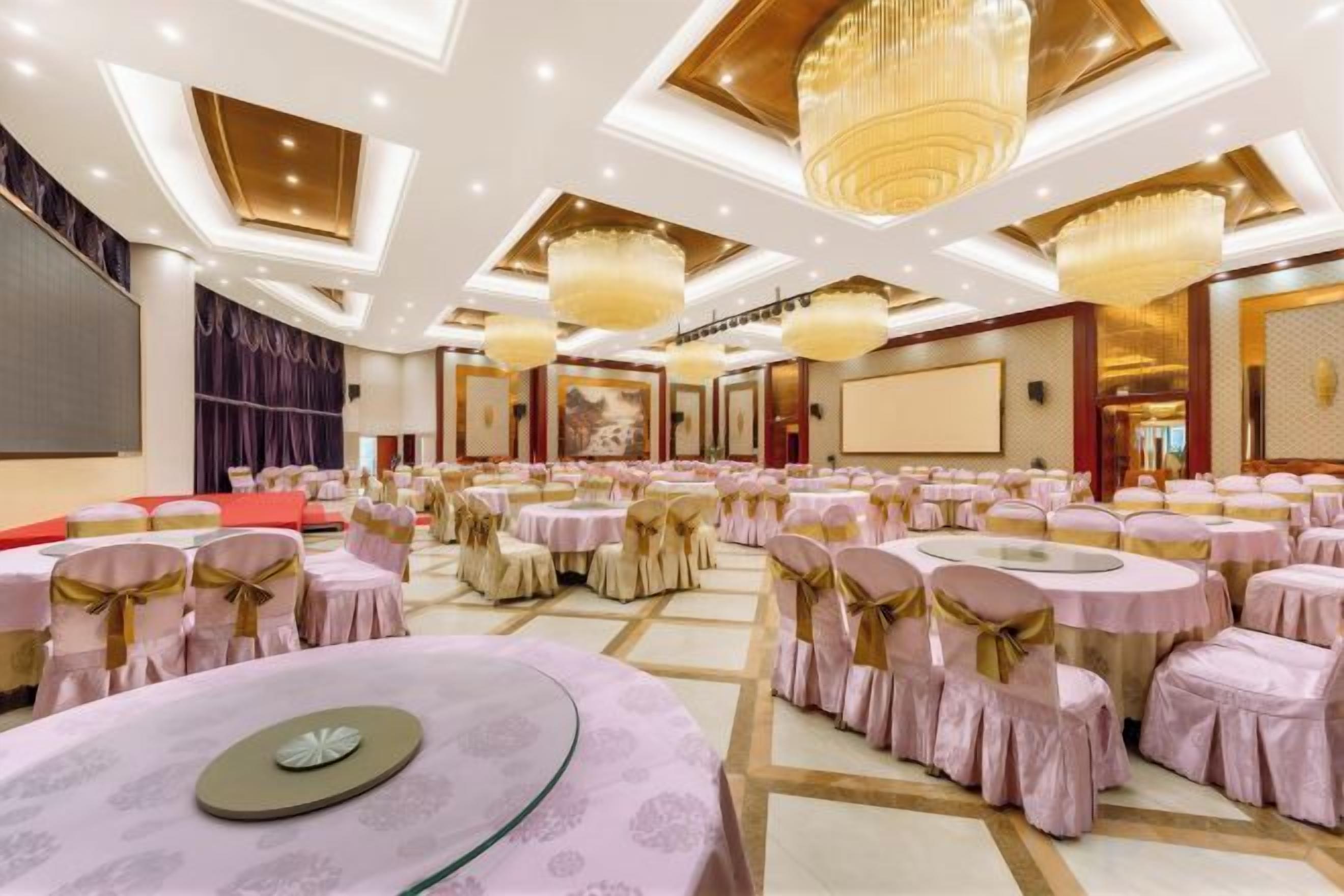 Un salón de banquetes con mesas redondas, sillas y una zona de escenario.