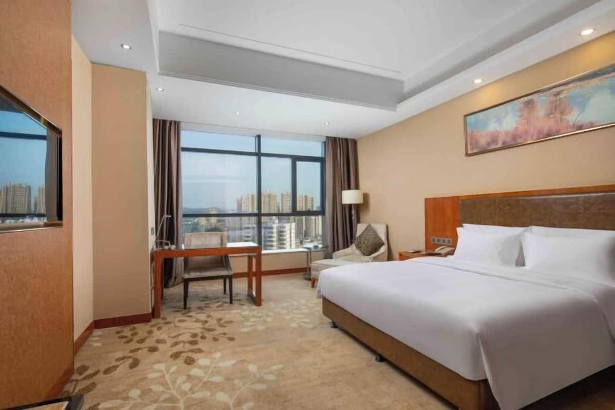 Habitación de hotel con una cama grande, un escritorio, una silla y una ventana con vista a la ciudad.