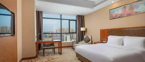 A hotel room with a large bed, a desk, a chair, and a window with a city view.