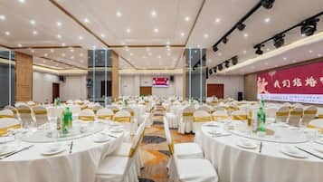 A banquet hall with round tables set for a formal event, equipped with chairs, tablecloths, and centerpieces.