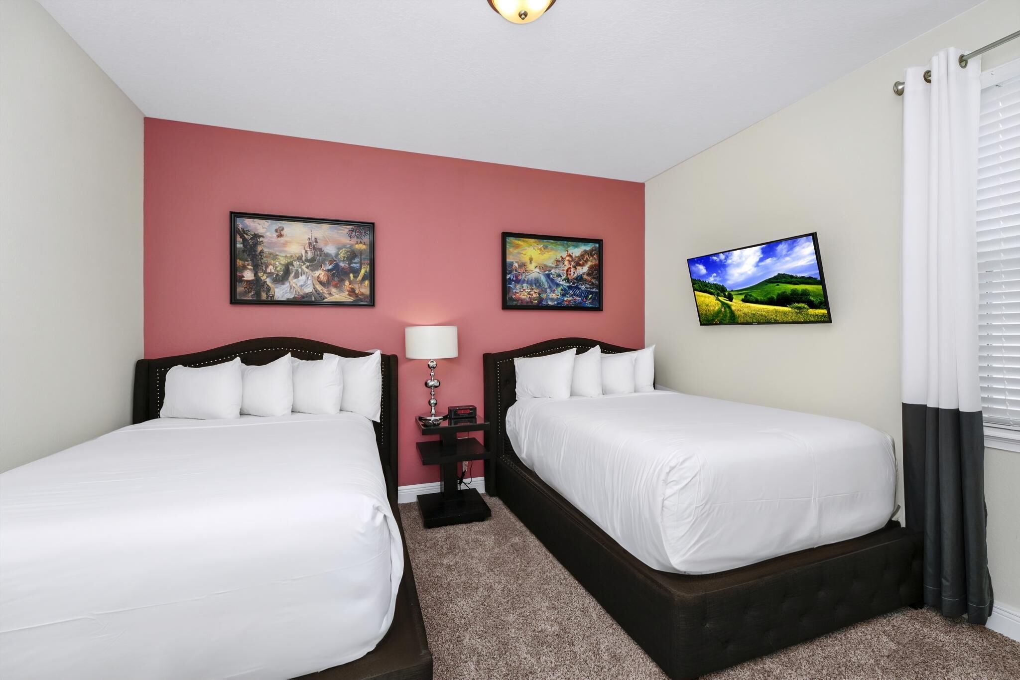 A hotel room with two beds, a red accent wall, and artwork.