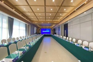 Un salón de conferencias con una larga mesa, sillas y un escenario al frente.