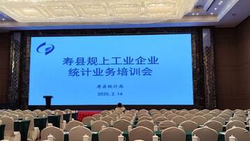 A conference room with a large screen displaying text, rows of chairs, and tables set for a meeting.