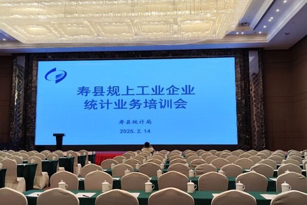 A conference room with a large screen displaying text, rows of chairs, and tables set for a meeting.