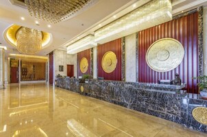 Zona de recepción de hotel con mostrador de mármol, paneles decorativos en la pared y una araña.
