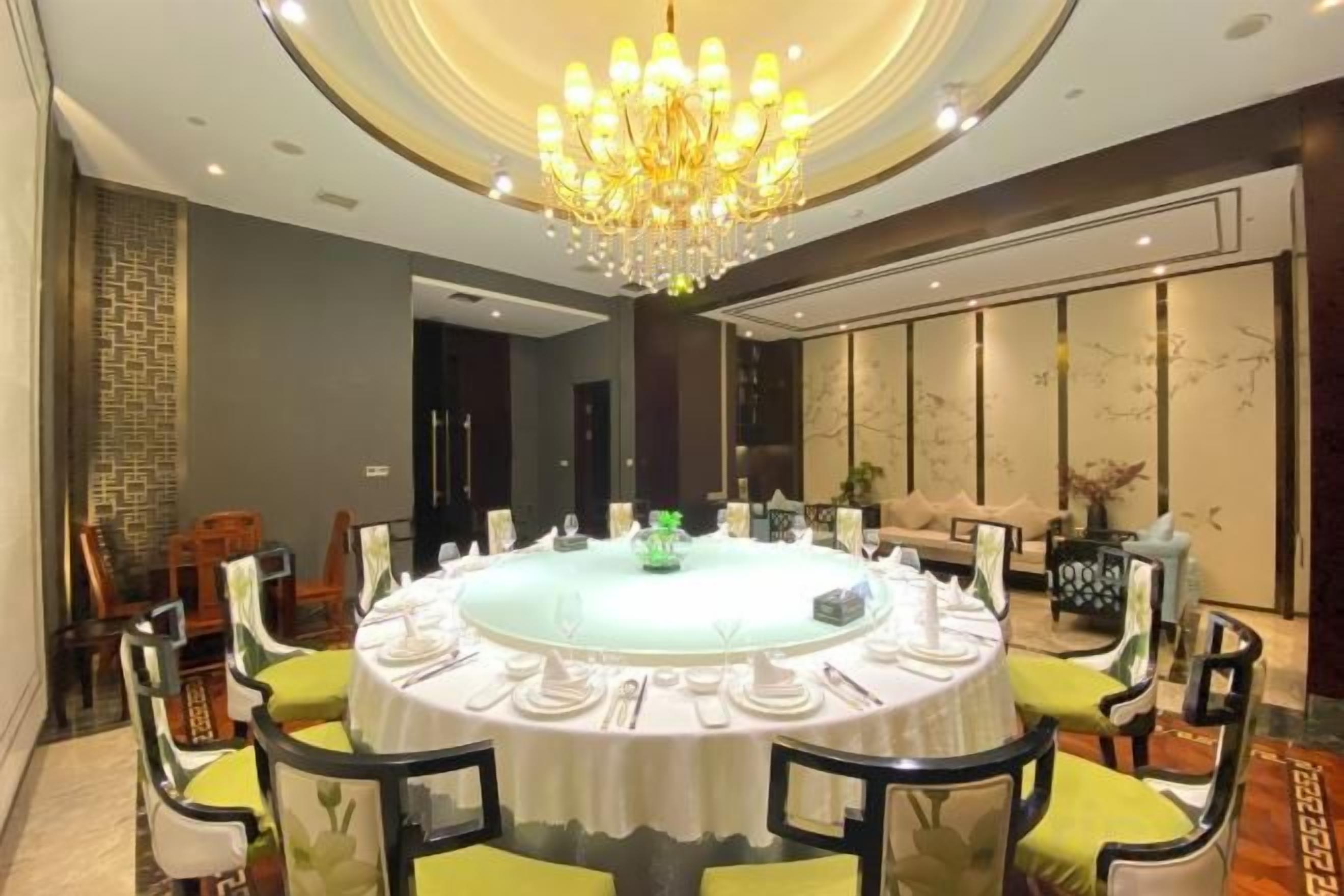 A round dining table with chairs, a chandelier, and a view of a room with a sofa and a plant.