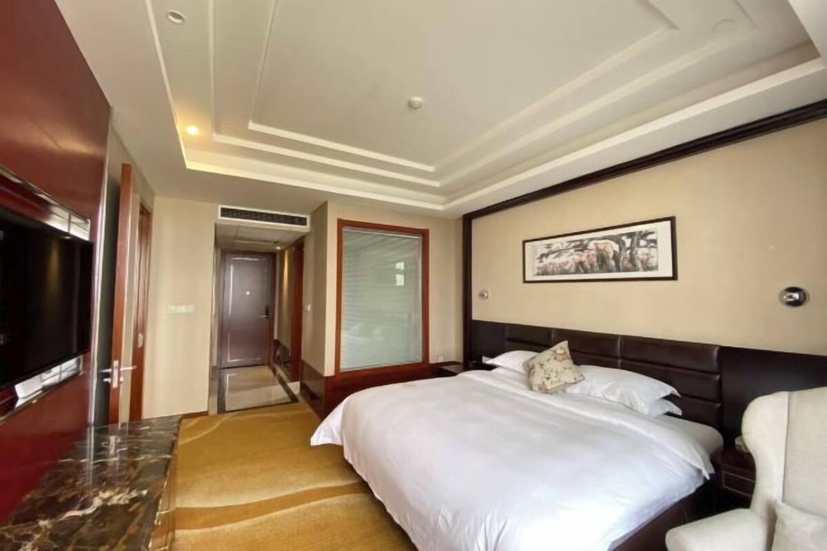 Ein Hotelzimmer mit Bett, Fernseher, einem gerahmten Bild an der Wand und Teppichboden.