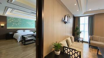 Una habitación de hotel moderna con piso de madera, una cama con ropa blanca, un sofá, una mesita con una planta y un reloj de pared.