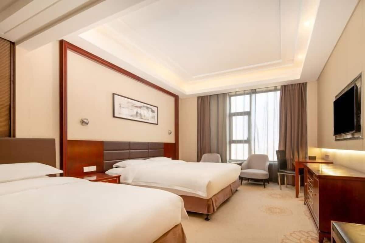 Ein Hotelzimmer mit zwei Betten, einem Schreibtisch, einem Sessel, einem Fernseher und einem Bild an der Wand.