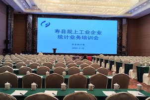 Un salón de conferencias con filas de sillas mirando hacia una pantalla grande que muestra una presentación.