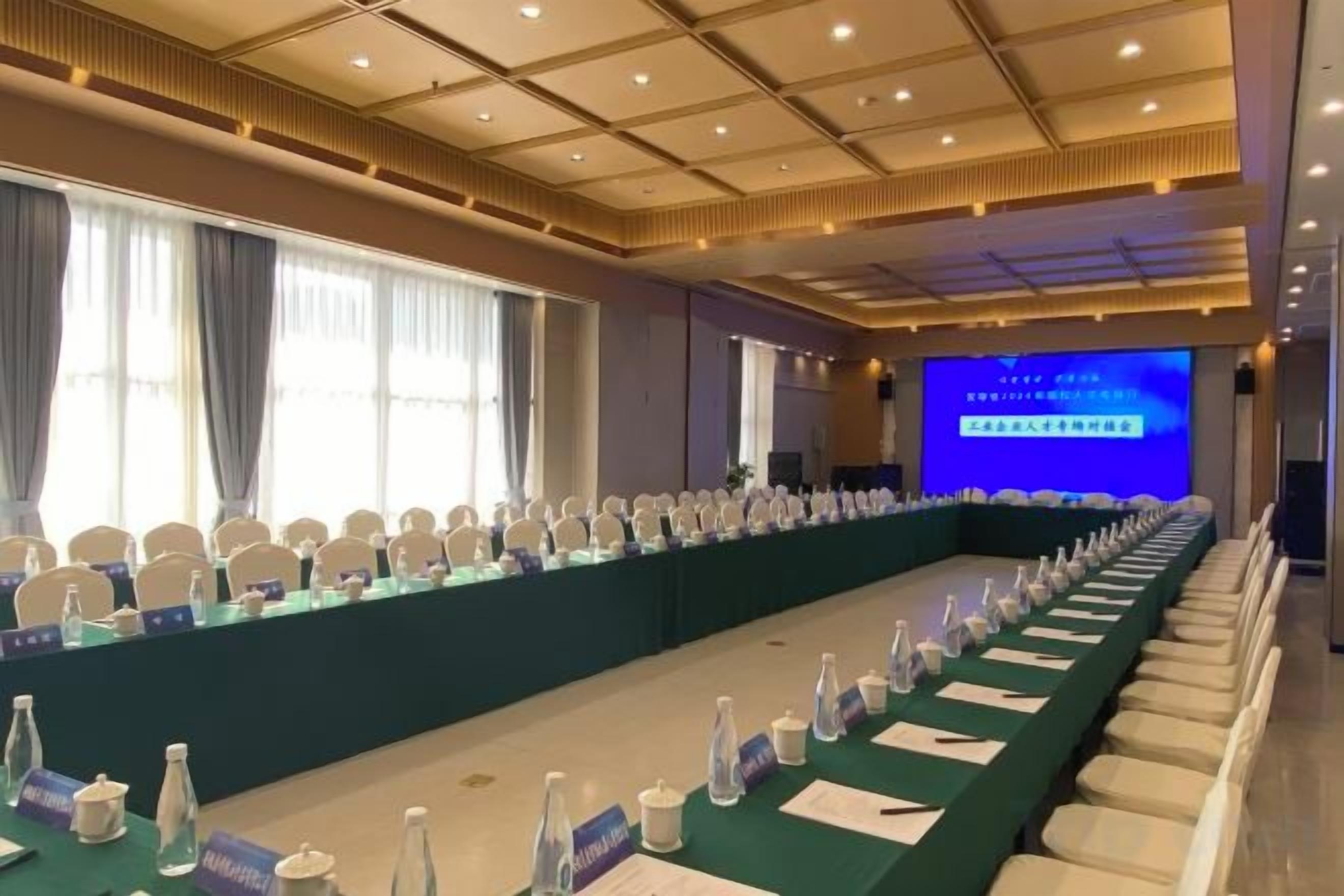 A conference room with a long table, chairs, nameplates, water bottles, and a screen displaying text.